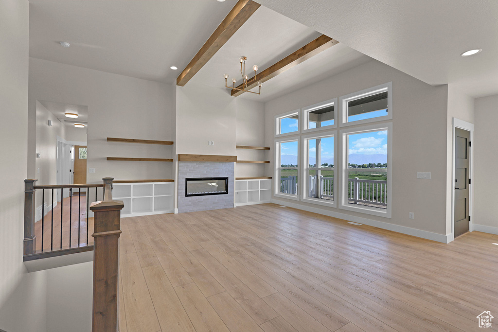Unfurnished living room featuring beamed ceiling, light wood-style floors, baseboards, a glass covered fireplace, and recessed lighting