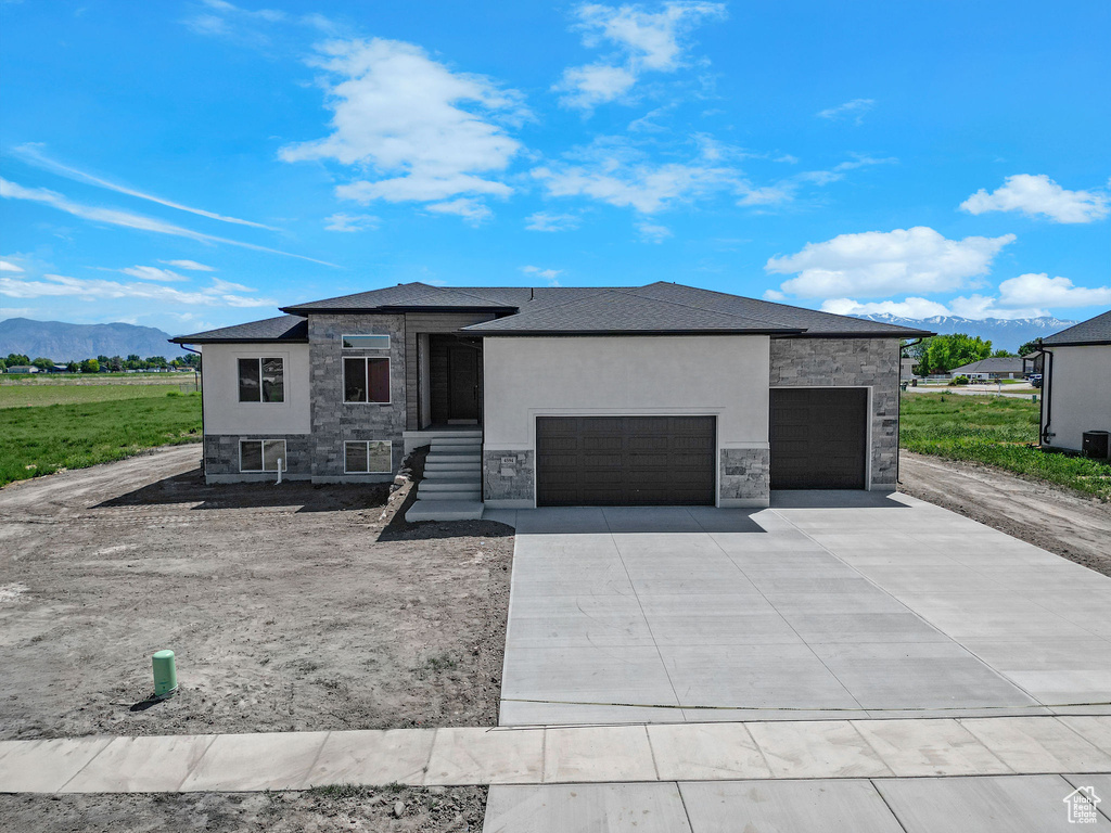 Prairie-style home featuring stone siding, an attached garage, a mountain view, and driveway
