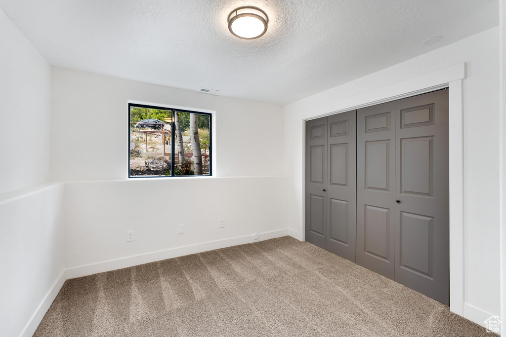 Unfurnished bedroom with carpet flooring, a textured ceiling, a closet, and baseboards