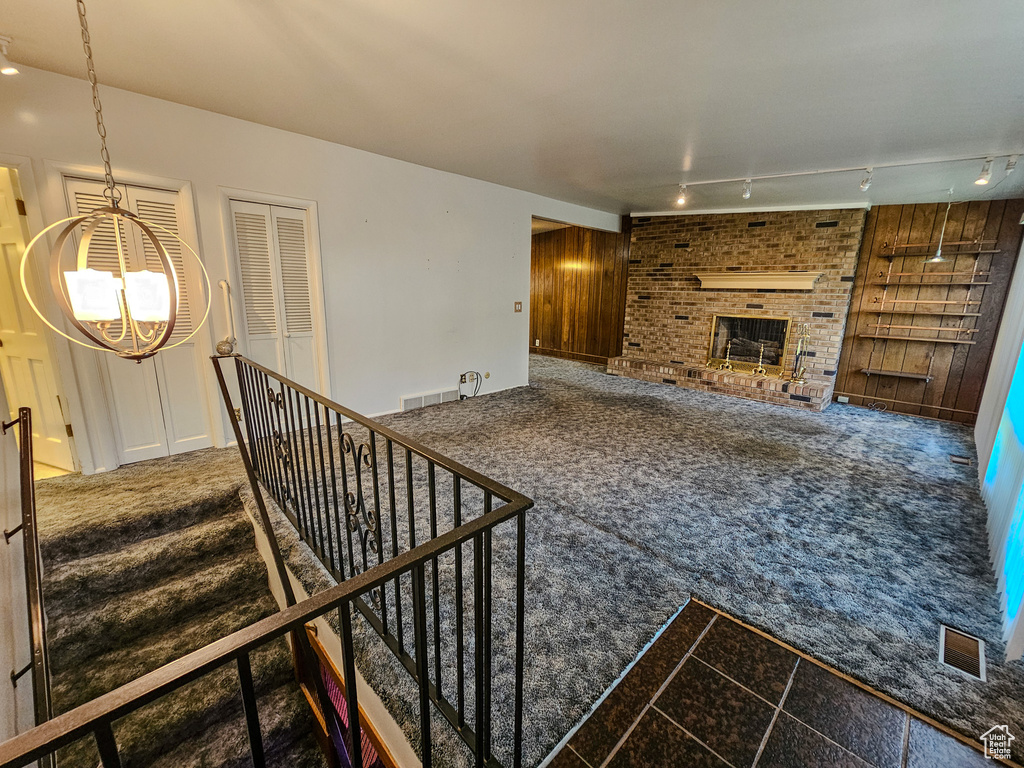Unfurnished living room featuring a chandelier, carpet, track lighting, and a fireplace