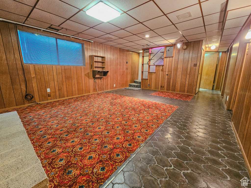 Finished below grade area featuring stairway, wooden walls, a paneled ceiling, stone finish flooring, and baseboards