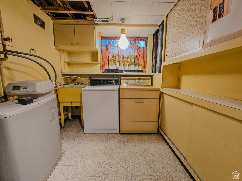 Kitchen featuring washer and dryer, light countertops, light floors, a sink, and decorative light fixtures