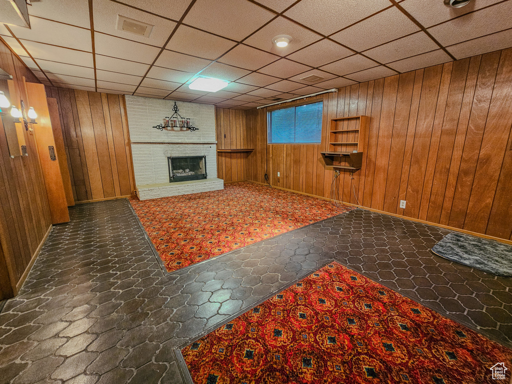 Unfurnished living room with wood walls, a fireplace, a paneled ceiling, and baseboards