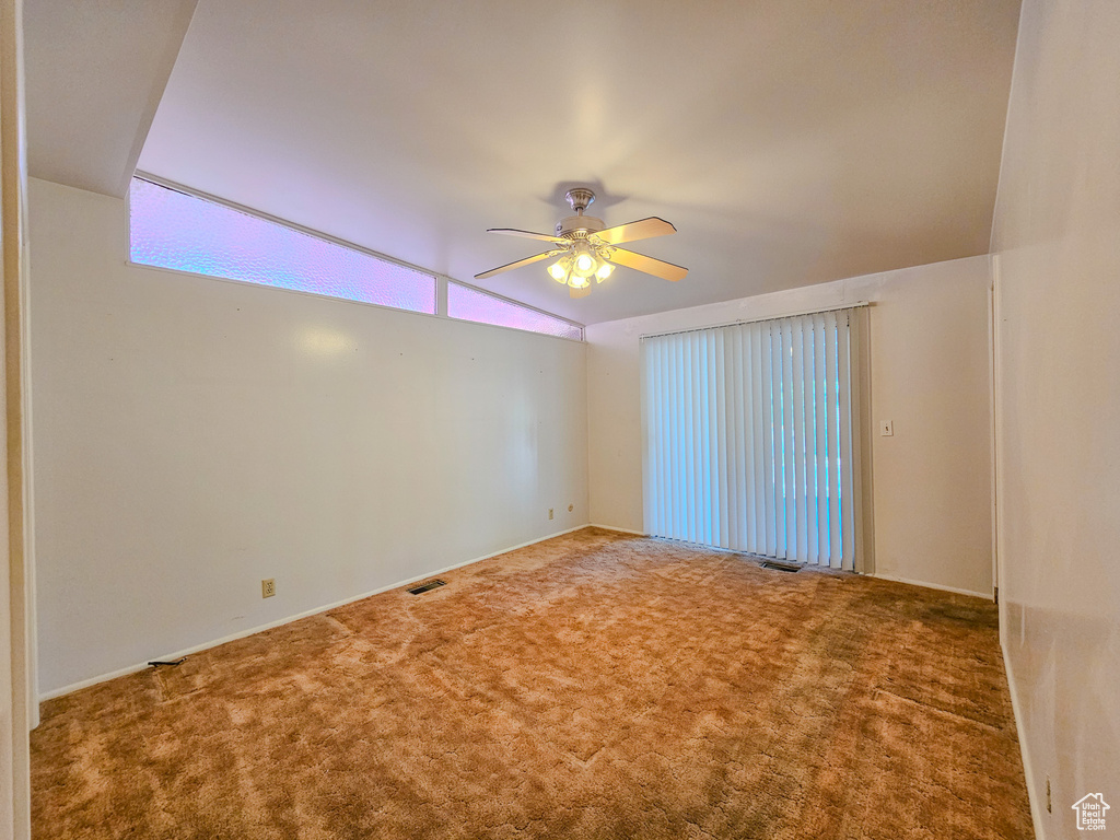 Carpeted empty room with a ceiling fan and vaulted ceiling