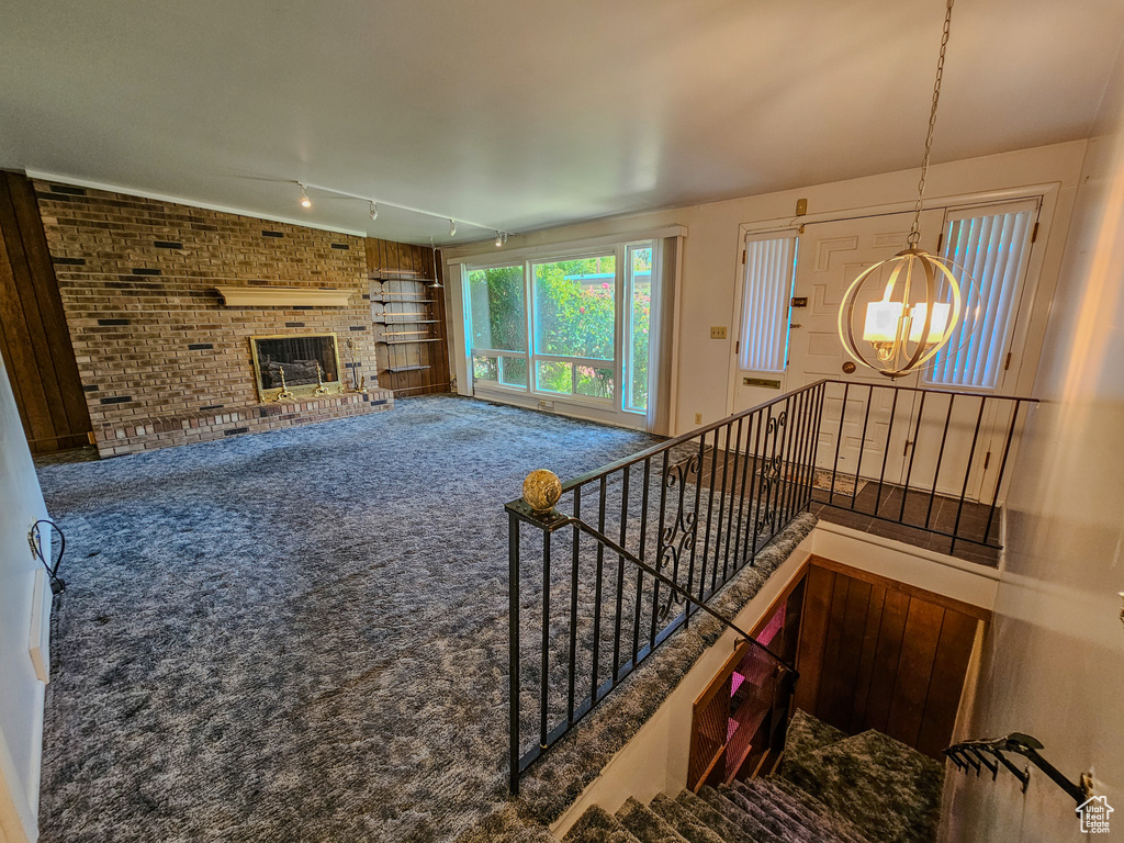 Unfurnished living room featuring a chandelier, carpet flooring, track lighting, and a brick fireplace