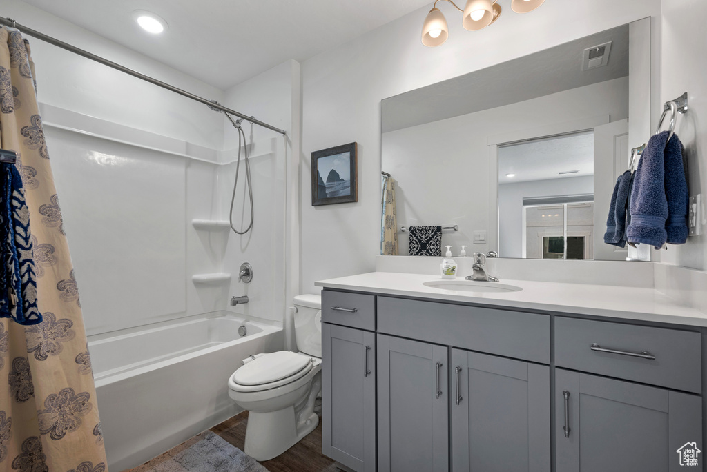 Bathroom featuring toilet, wood finished floors, vanity, and shower / bath combination with curtain