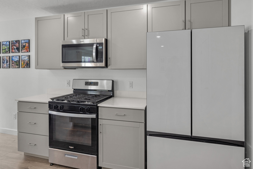 Kitchen with stainless steel appliances, gray cabinets, light countertops, and light wood finished floors