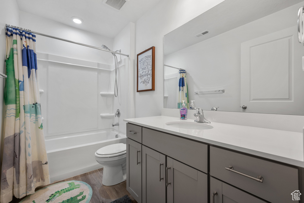 Bathroom with vanity, wood finished floors, shower / bath combination with curtain, toilet, and recessed lighting