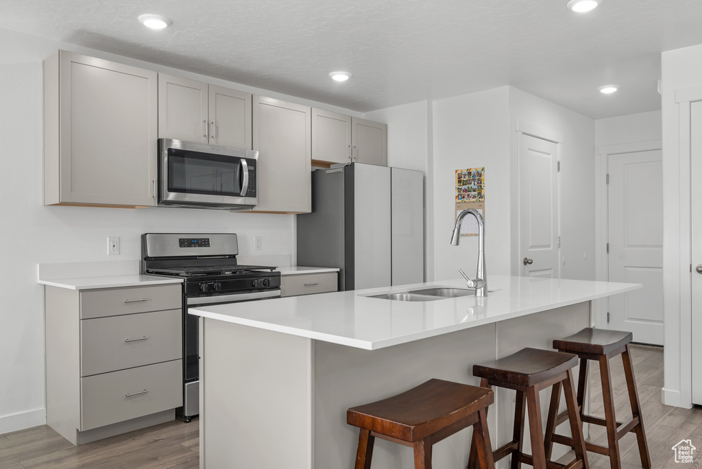 Kitchen featuring stainless steel appliances, a sink, gray cabinetry, light wood-type flooring, and a breakfast bar area