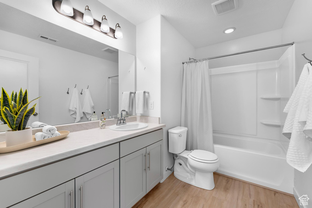 Full bathroom featuring vanity, wood finished floors, toilet, and shower / tub combo with curtain