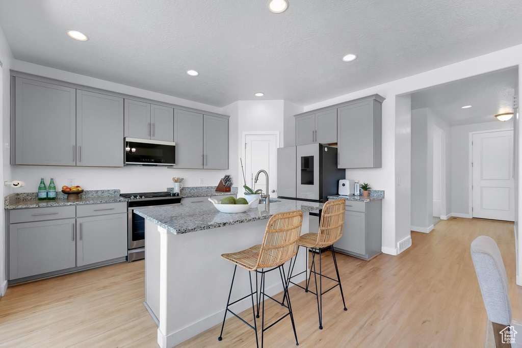 Kitchen featuring appliances with stainless steel finishes, gray cabinets, light wood-style floors, light stone countertops, and recessed lighting