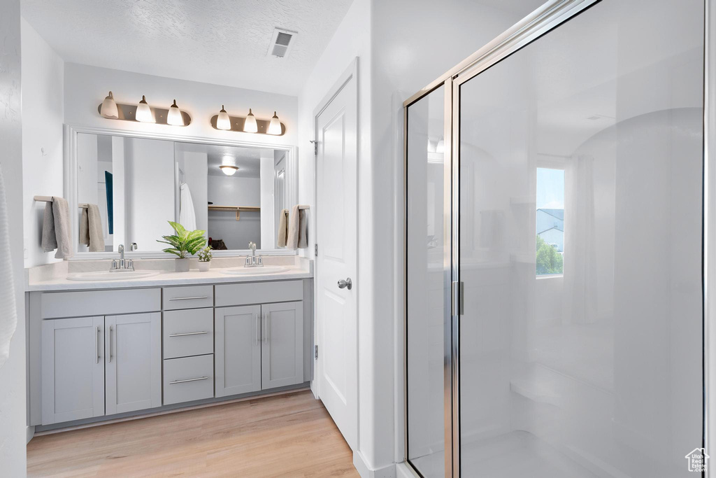 Bathroom featuring double vanity, a stall shower, wood finished floors, and a textured ceiling