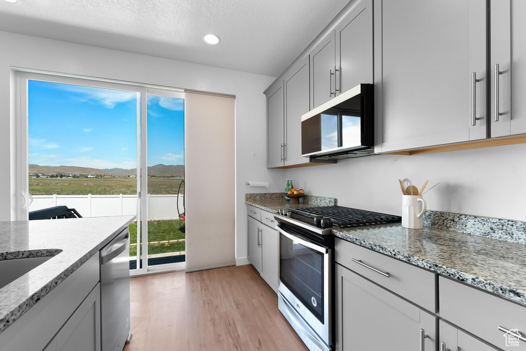 Kitchen with stainless steel appliances, a mountain view, gray cabinetry, light wood-style flooring, and light stone countertops
