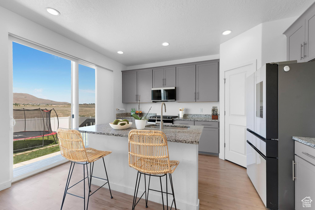 Kitchen featuring freestanding refrigerator, gray cabinets, light stone countertops, an island with sink, and recessed lighting