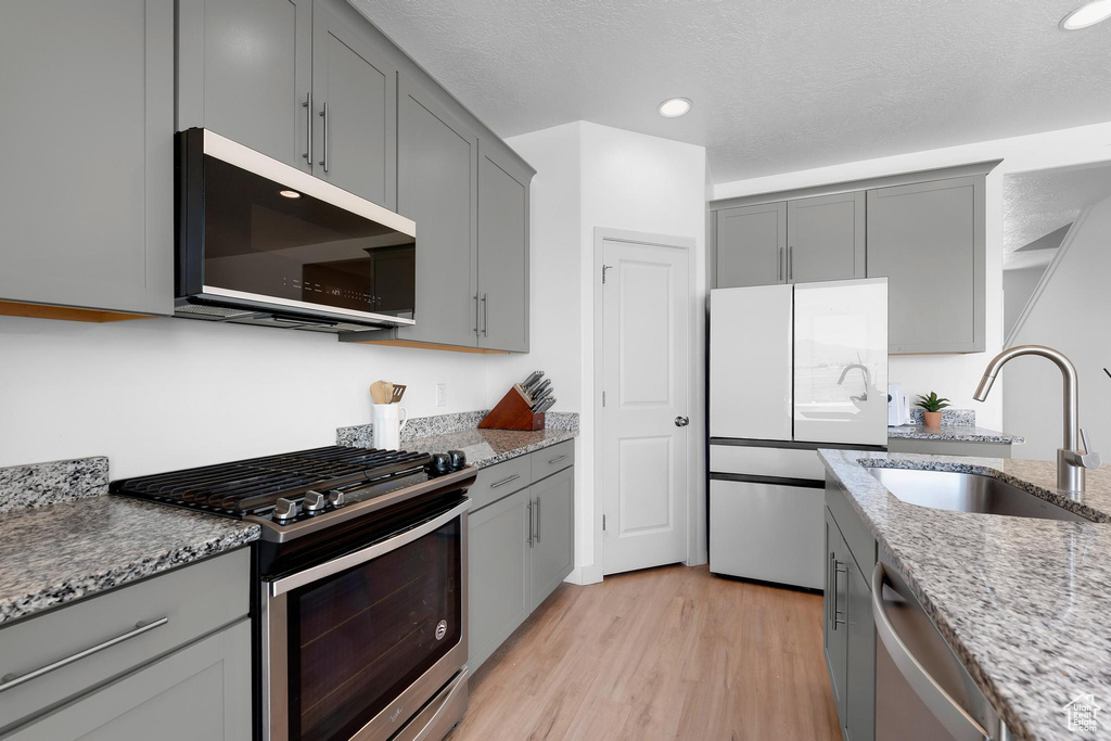 Kitchen featuring stainless steel appliances, gray cabinetry, a sink, light stone counters, and light wood-type flooring