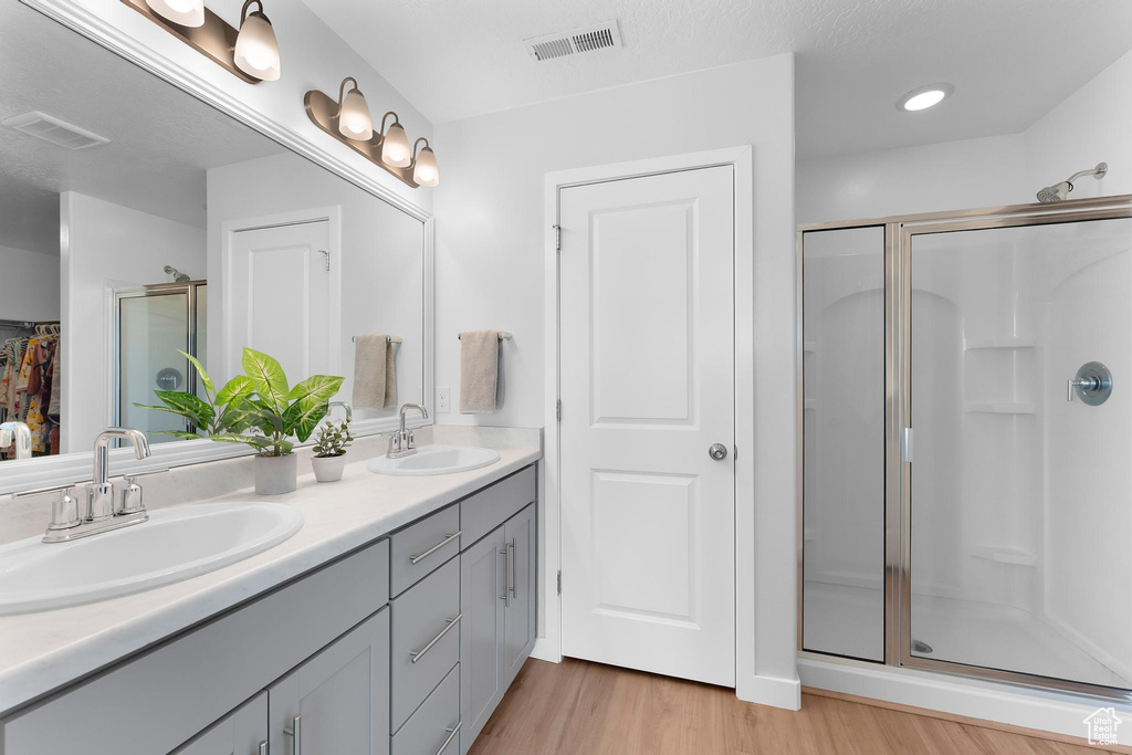 Full bath with double vanity, a stall shower, wood finished floors, and a closet