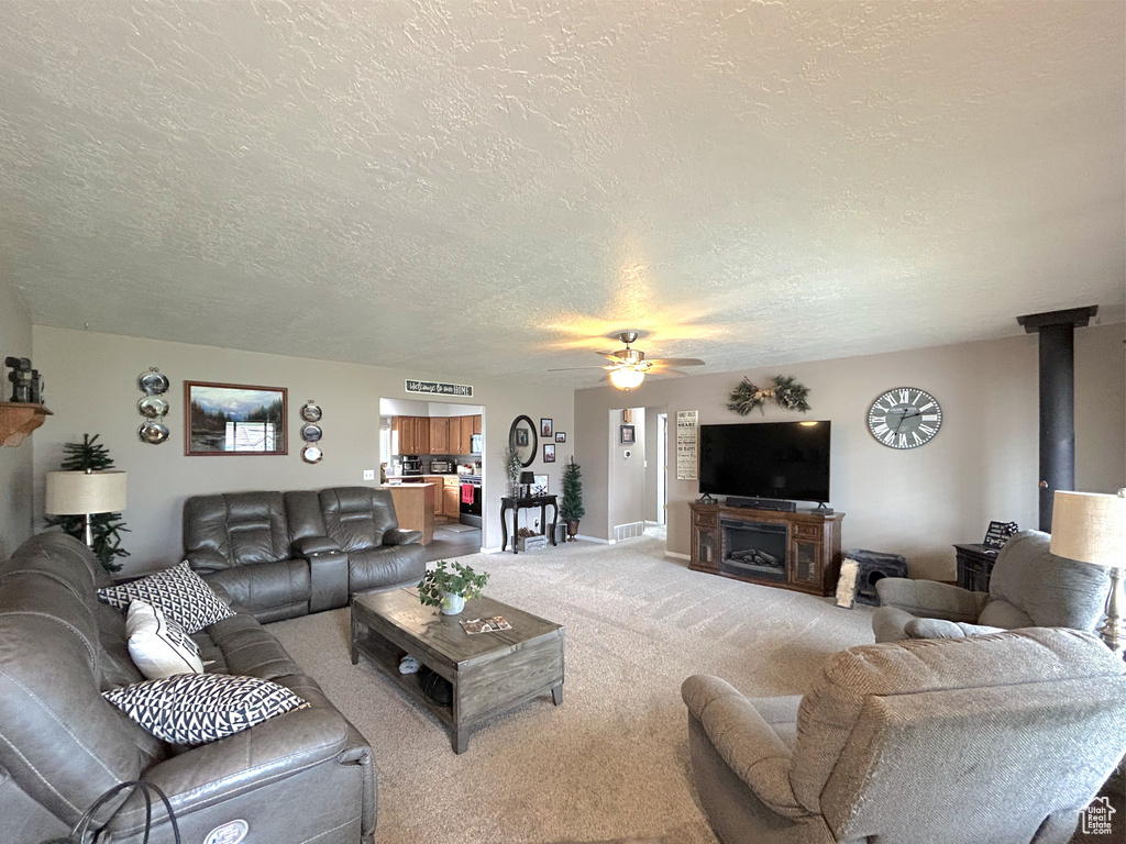 Living room with a textured ceiling, ceiling fan, light colored carpet, and baseboards