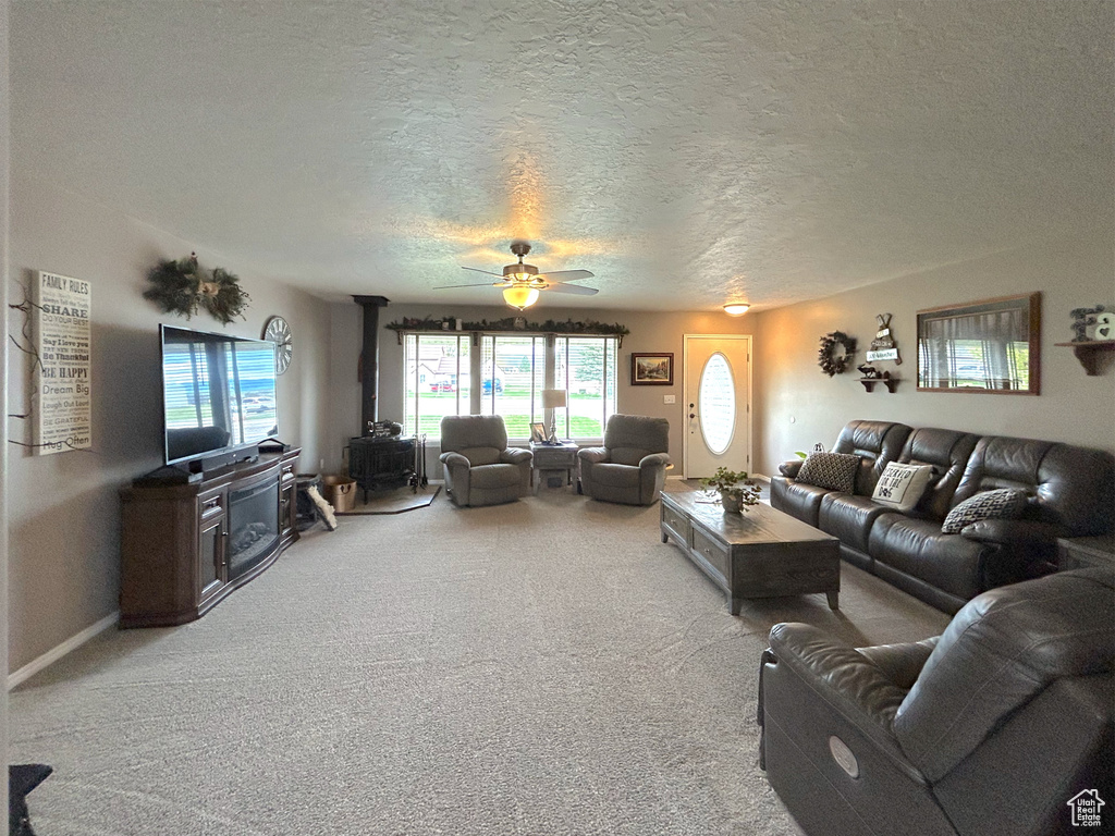 Carpeted living room with a wood stove, a textured ceiling, healthy amount of natural light, and ceiling fan