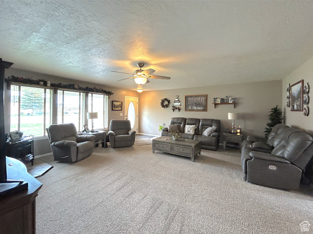 Living room with a textured ceiling, carpet flooring, and ceiling fan
