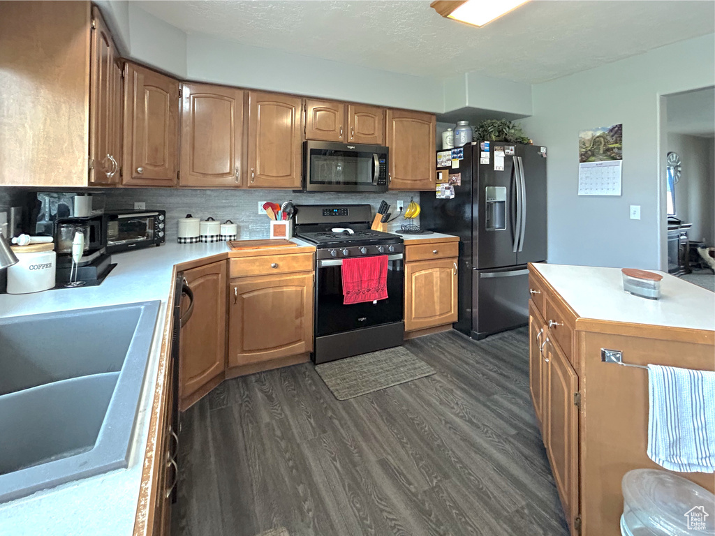 Kitchen featuring stainless steel range with gas cooktop, black refrigerator with ice dispenser, a sink, light countertops, and dark wood-style flooring