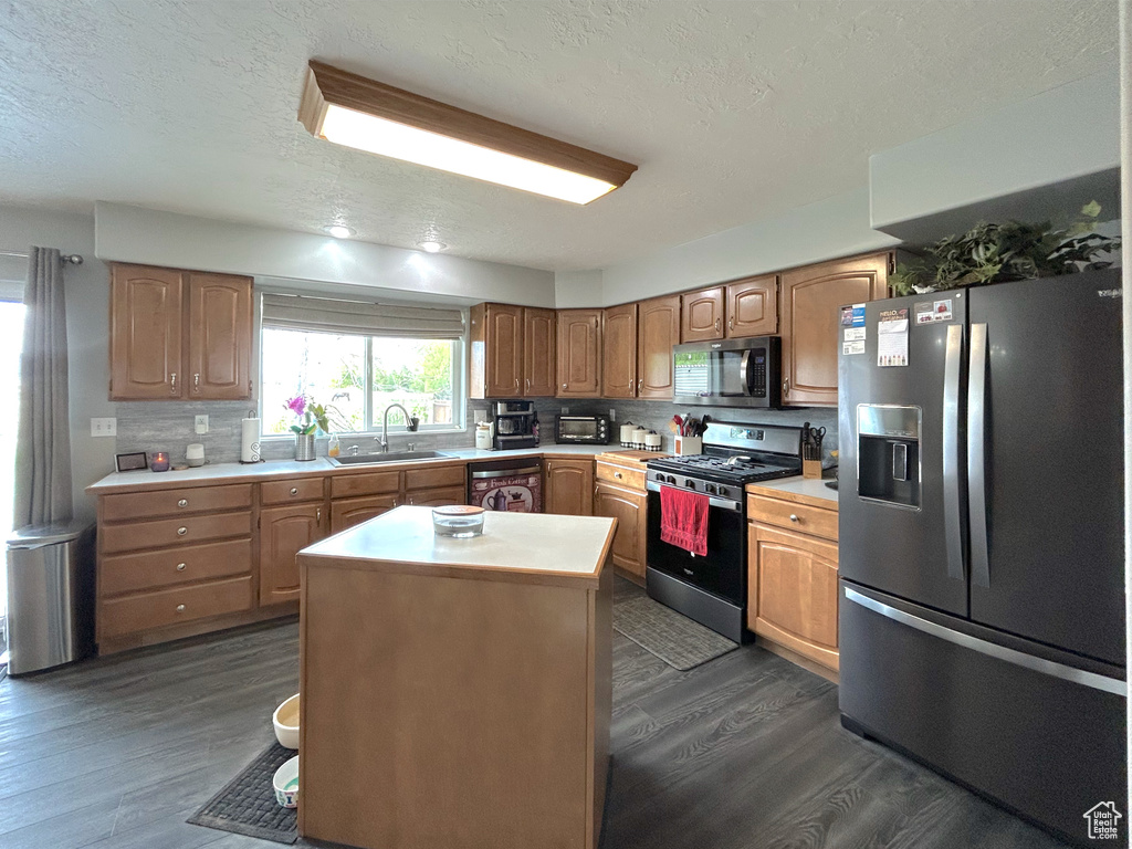Kitchen featuring appliances with stainless steel finishes, a sink, dark wood finished floors, light countertops, and a textured ceiling