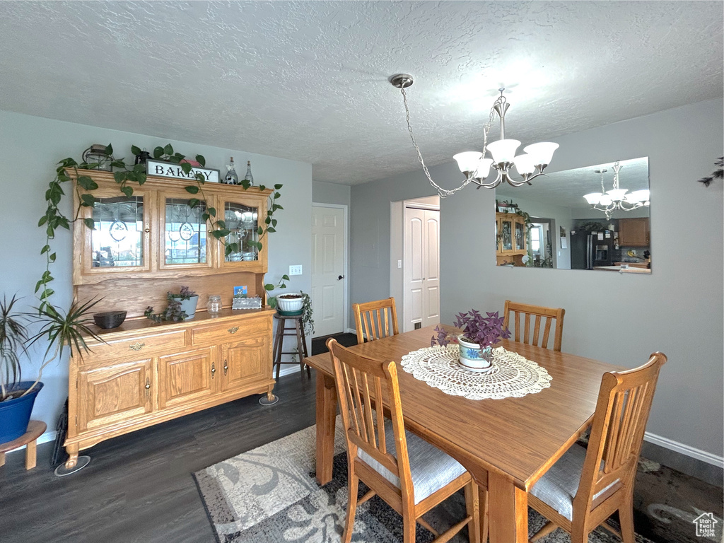 Dining room with a chandelier, dark wood-style flooring, a textured ceiling, and baseboards