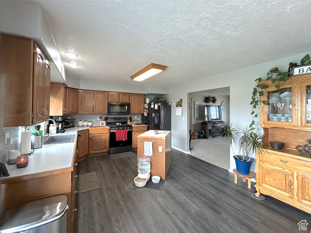 Kitchen with black appliances, a sink, light countertops, a kitchen island, and a textured ceiling