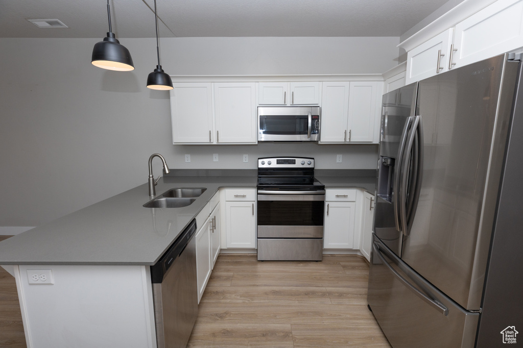Kitchen featuring appliances with stainless steel finishes, a sink, a peninsula, light wood-style floors, and white cabinetry