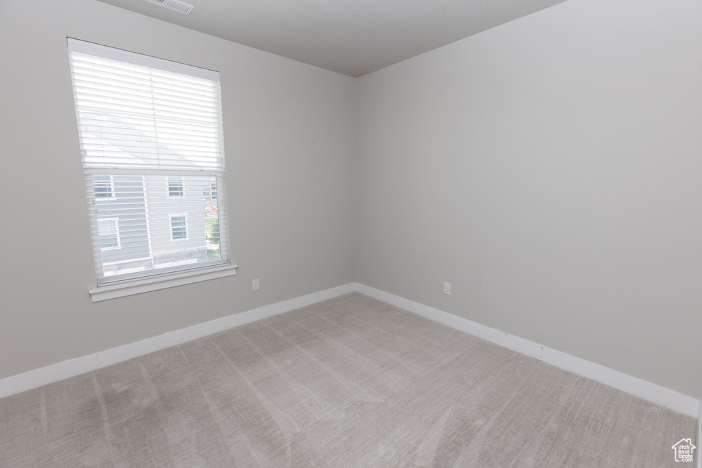 Empty room featuring healthy amount of natural light, light carpet, and baseboards