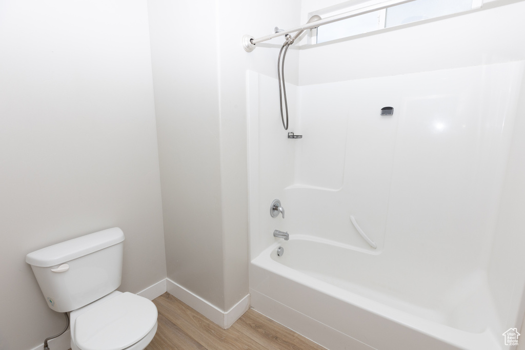 Bathroom with wood finished floors, toilet, baseboards, and shower / bath combination