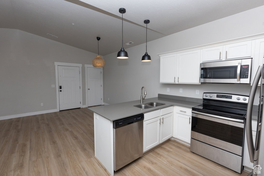 Kitchen featuring stainless steel appliances, a sink, lofted ceiling, light wood-type flooring, and white cabinetry
