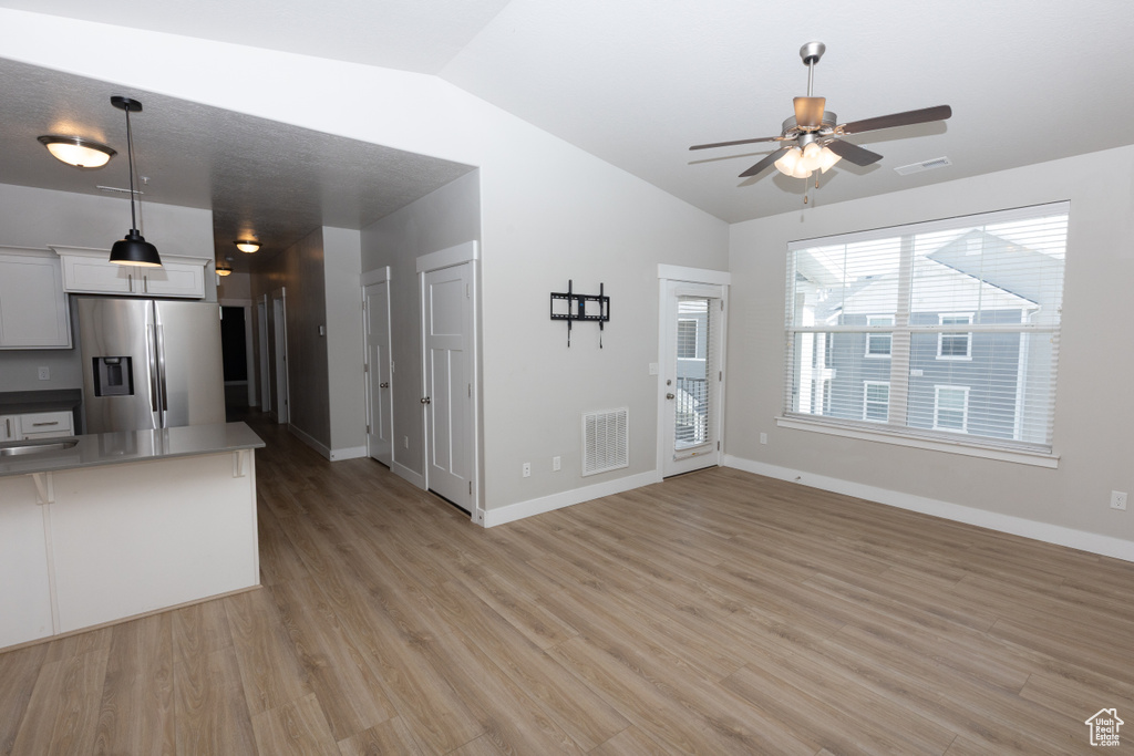 Unfurnished living room featuring lofted ceiling, ceiling fan, light wood-style flooring, and baseboards