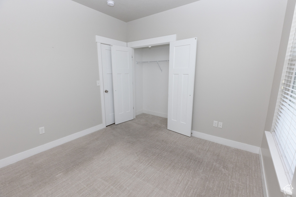 Unfurnished bedroom featuring light colored carpet, a closet, and baseboards