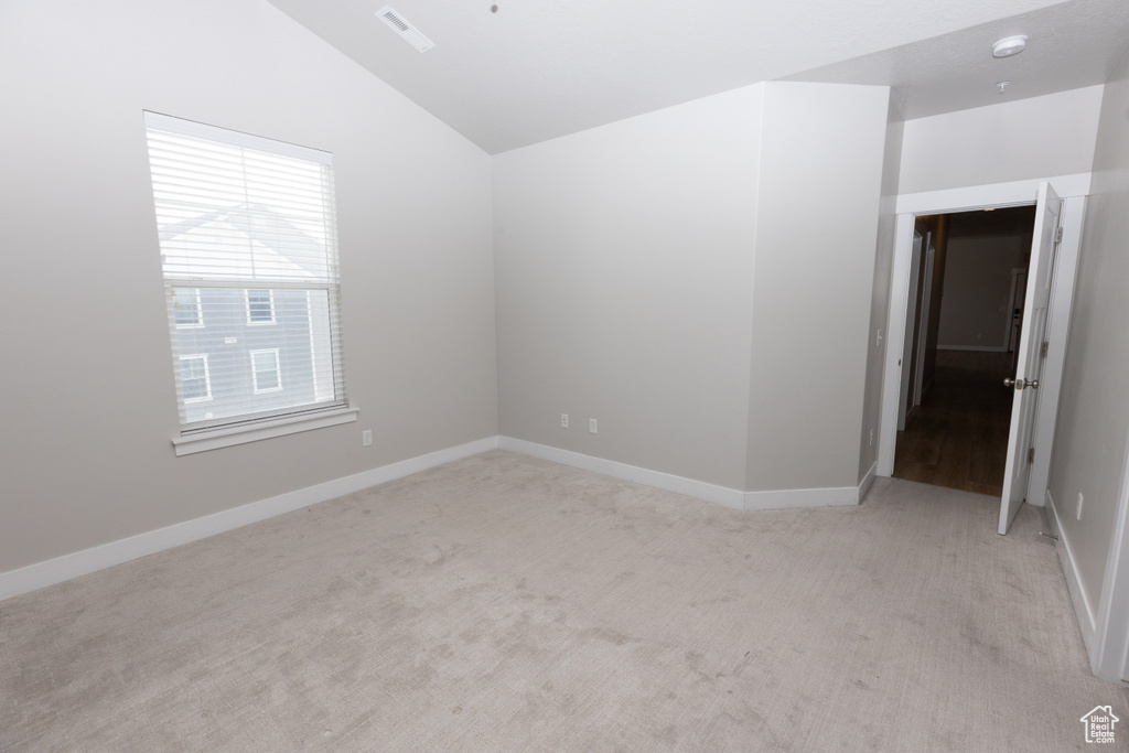 Spare room featuring lofted ceiling, light colored carpet, and baseboards