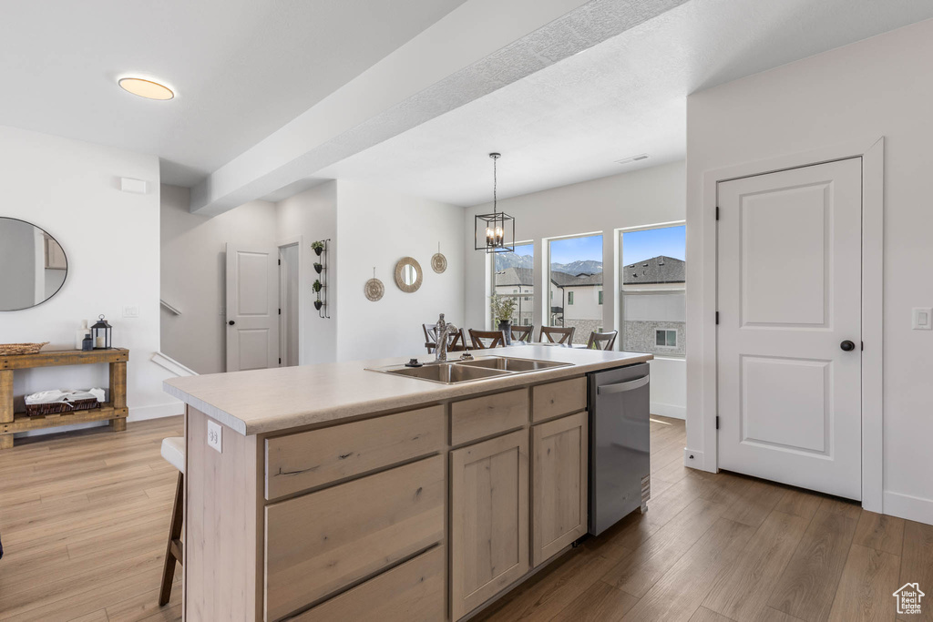 Kitchen with stainless steel dishwasher, a sink, an island with sink, light wood-type flooring, and light countertops