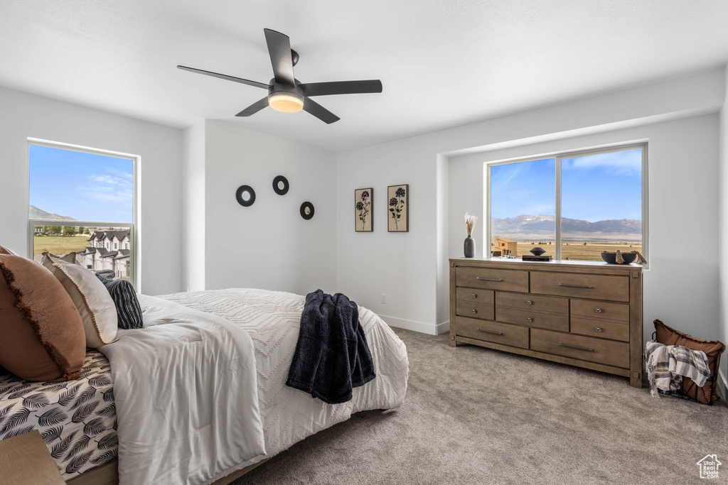 Bedroom with light colored carpet, multiple windows, a ceiling fan, and a mountain view