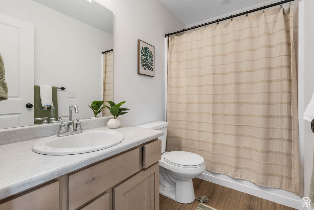 Bathroom featuring toilet, vanity, wood finished floors, and shower / bath combination with curtain