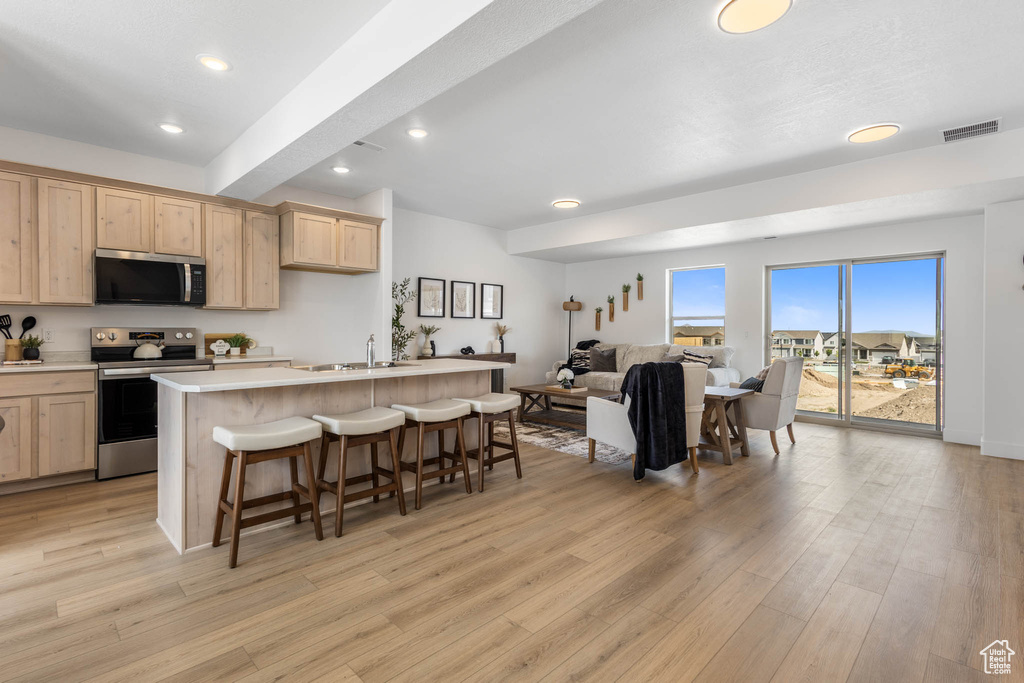 Kitchen featuring stainless steel appliances, light brown cabinetry, a sink, open floor plan, and a kitchen bar