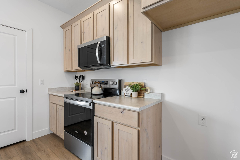Kitchen with stainless steel appliances, light brown cabinetry, light countertops, and light wood-style flooring