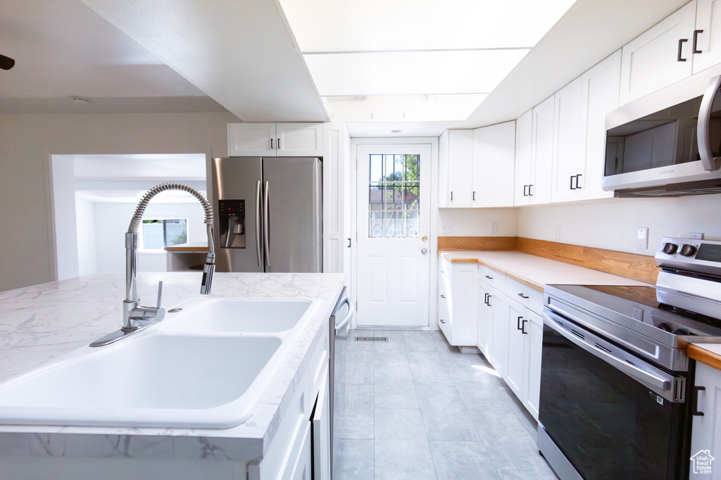 Kitchen featuring appliances with stainless steel finishes, a sink, white cabinetry, and light stone countertops