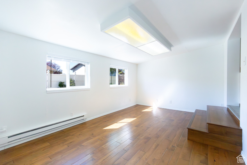 Empty room featuring a baseboard radiator, wood finished floors, and baseboards