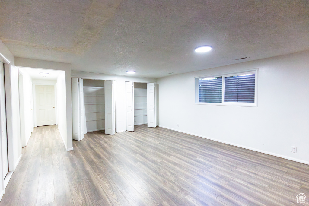 Unfurnished bedroom featuring wood finished floors, baseboards, a textured ceiling, two closets, and recessed lighting