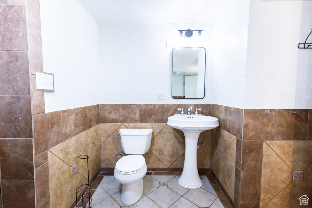Half bath featuring toilet, tile walls, wainscoting, and tile patterned floors