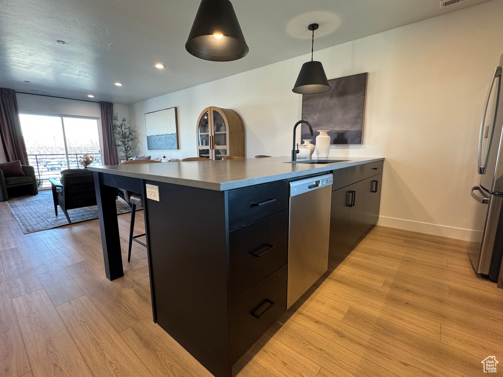 Kitchen featuring appliances with stainless steel finishes, a sink, open floor plan, light wood finished floors, and baseboards