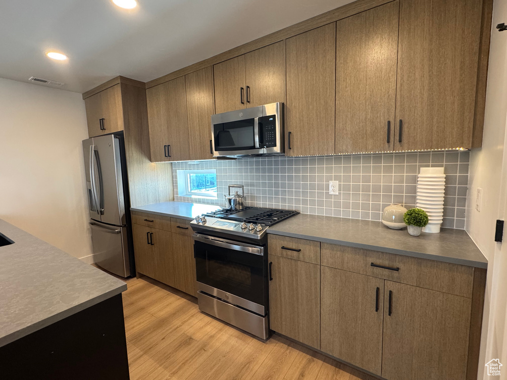 Kitchen featuring appliances with stainless steel finishes, light wood finished floors, decorative backsplash, and recessed lighting