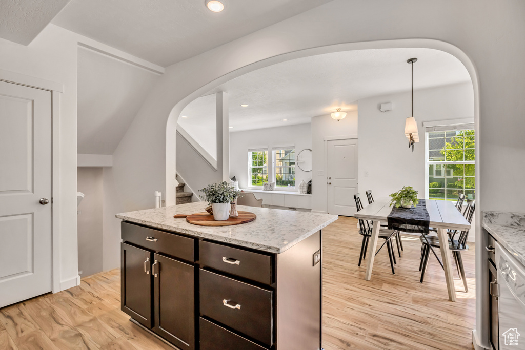 Kitchen with light wood-style flooring, pendant lighting, arched walkways, light stone counters, and dark brown cabinets