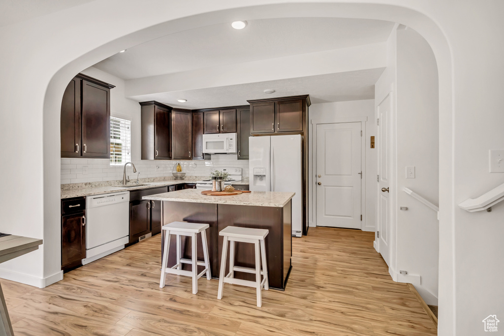 Kitchen with white appliances, dark brown cabinetry, light wood-type flooring, decorative backsplash, and a kitchen island