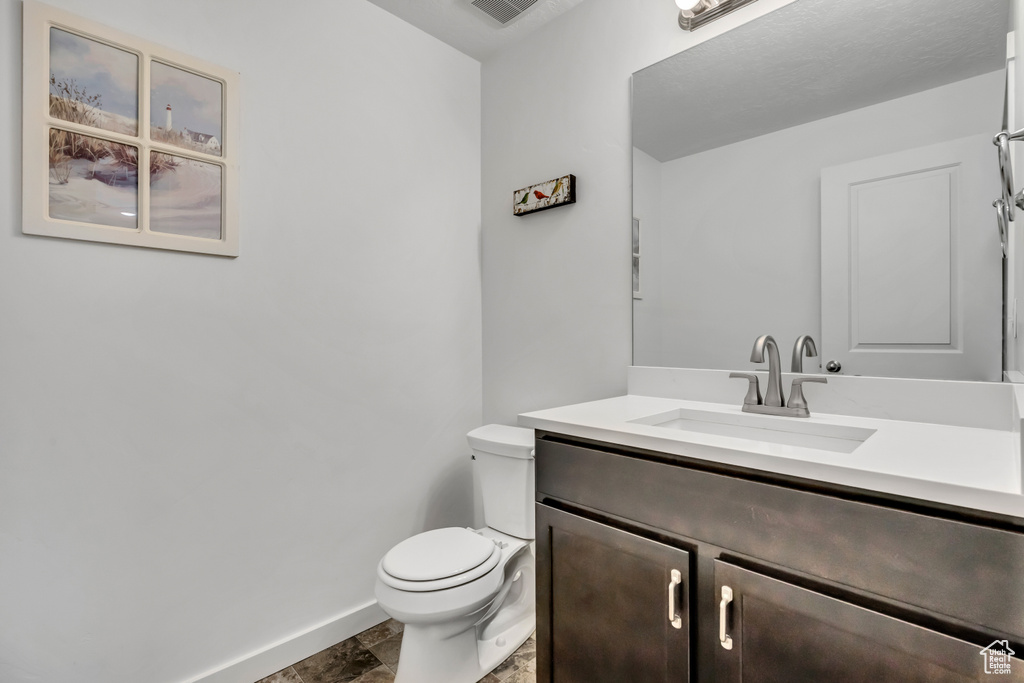 Half bath with baseboards, vanity, toilet, and stone finish floors