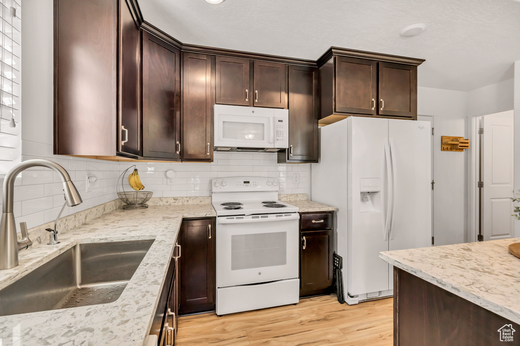 Kitchen featuring white appliances, a sink, light wood-style floors, and dark brown cabinetry
