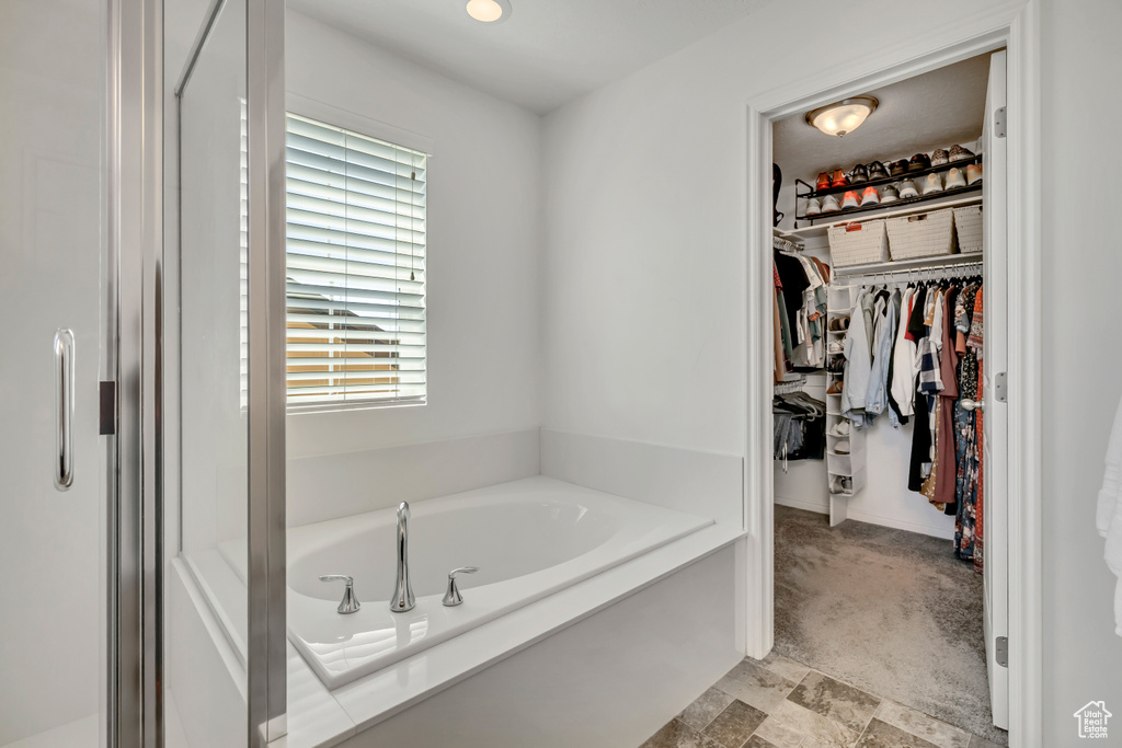 Bathroom featuring a bath, a walk in closet, and stone finish floors
